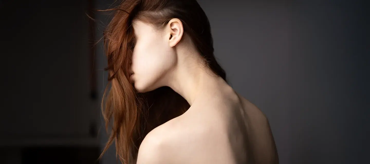 A woman with beautiful healthy hair falling over her face showing the slender and pale back of her neck